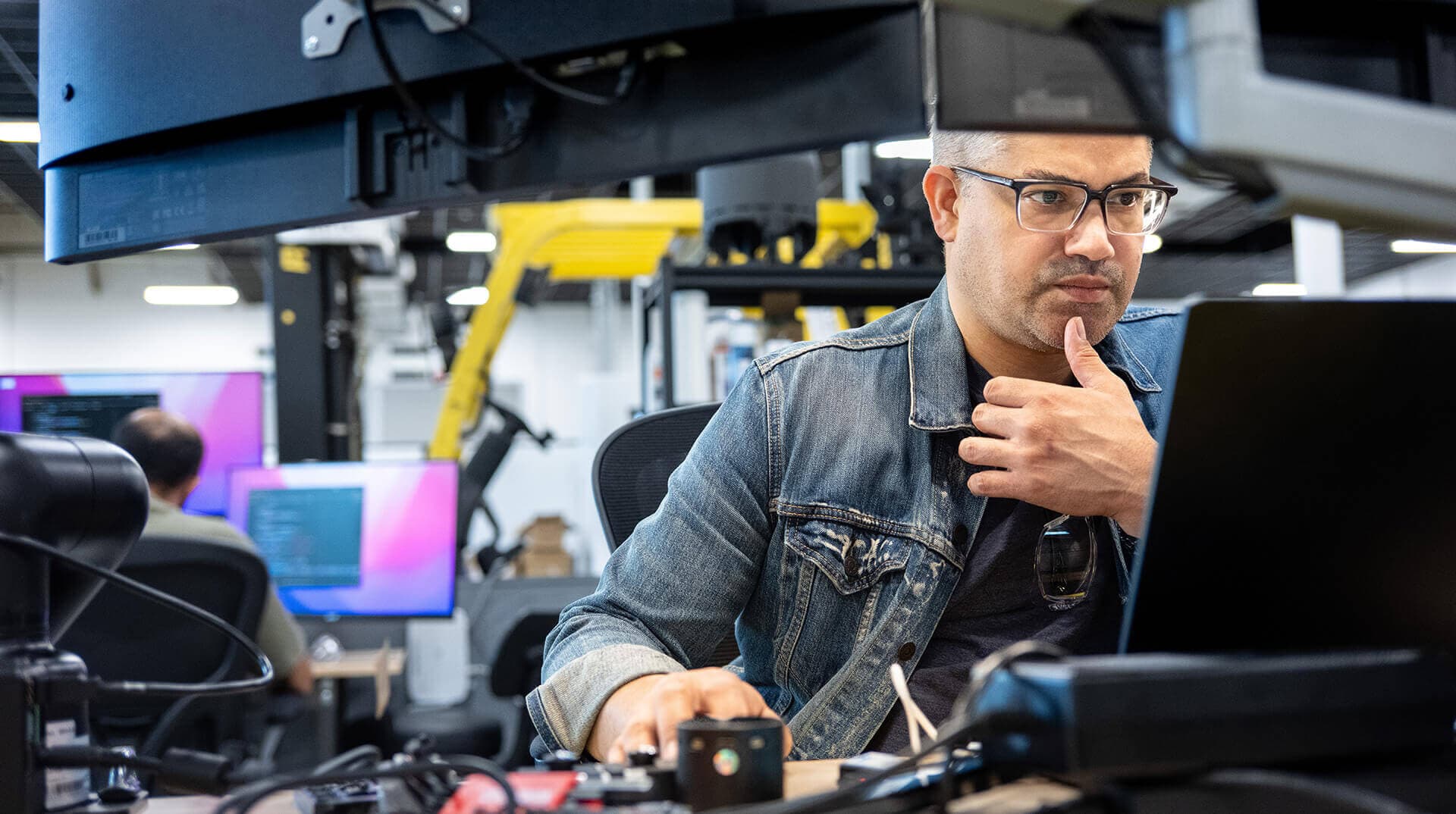 A Greentown founder focused at a hardware prototyping station, surrounded by robotics, monitors, and engineering equipment